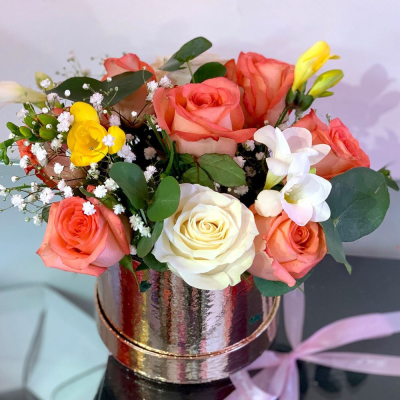 Coral Bliss Hatbox - A delightful arrangement in a hatbox, featuring warm coral and cream tones, accented with fresh greenery. This compact design is perfect for gifting and adds a touch of elegance to any space.